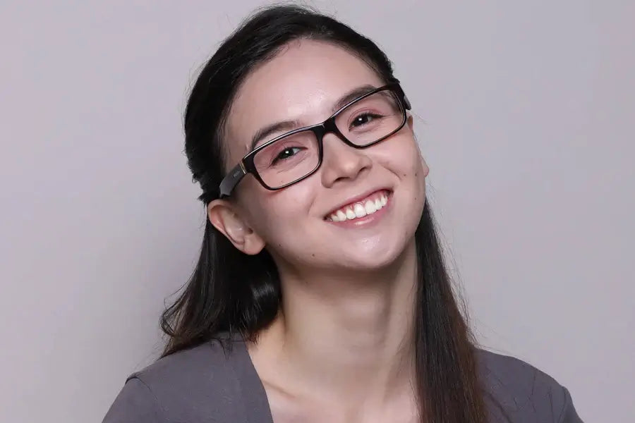 Smiling young woman wearing stylish glasses, showcasing a confident and joyful expression against a neutral background.